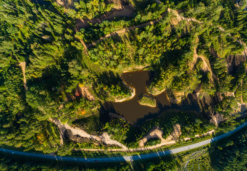 Aerial view of a small pond surrounded by dense forest dirt trails and a road in Latvia. Aerial view of a small pond surrounded by dense forest dirt trails and a road in Latvia.