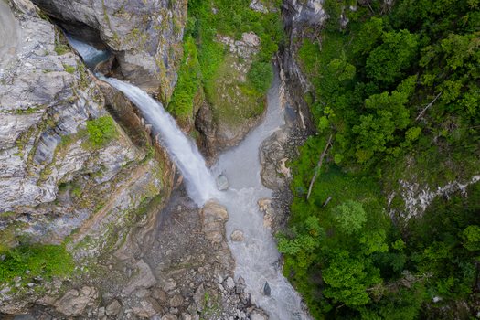 Aerial view of a powerful waterfall cascading into a rocky canyon surrounded by lush green forest and rugged cliffs in Nepal.