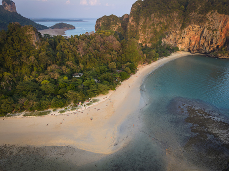 Aerial view of the beach meeting the turquoise sea cliffs rising majestically and dense green forest Krabi Thailand.