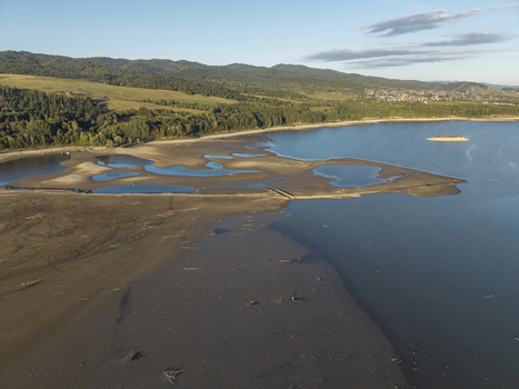 Aerial view of a reservoir with low water levels revealing sandy banks and small islands surrounded by forested hills and a clear blue sky in Poland. Aerial view of a reservoir with low water levels revealing sandy banks and small islands surrounded by forested hills and a clear blue sky in Poland.