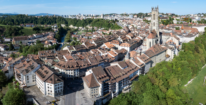 Aerial view of St Nicolas Cathedral rising above the historic old town rooftops and the Sarine river valley under a clear sky in Fribourg Fribourg Switzerland. Aerial view of St Nicolas Cathedral rising above the historic old town rooftops and the Sarine river valley under a clear sky in Fribourg Fribourg Switzerland.