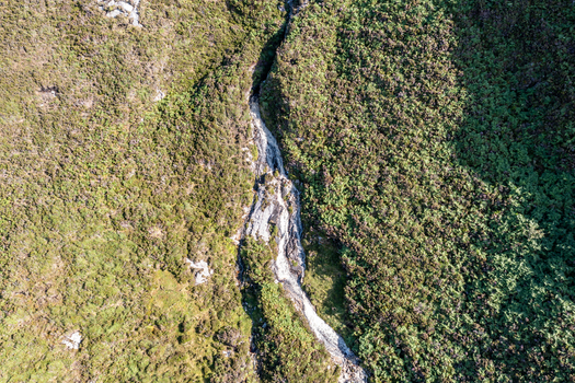 Aerial view of a narrow waterfall flowing through a rocky crevice surrounded by lush green hills and rugged terrain at An Port in Ardara County Donegal Ireland.