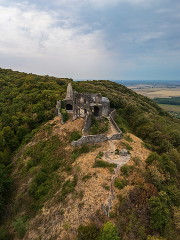 Aerial view of Somlo Castle ruins on a wooded hilltop in Hungary under cloudy skies above Aerial view of Somlo Castle ruins on a wooded hilltop in Hungary under cloudy skies above