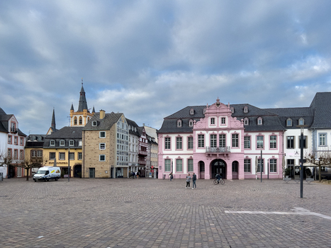 View of the historic Hauptmarkt square featuring the pink Steipe building traditional half timbered houses and cobblestone pavement under a cloudy sky in Trier Rheinland Pfalz Germany.