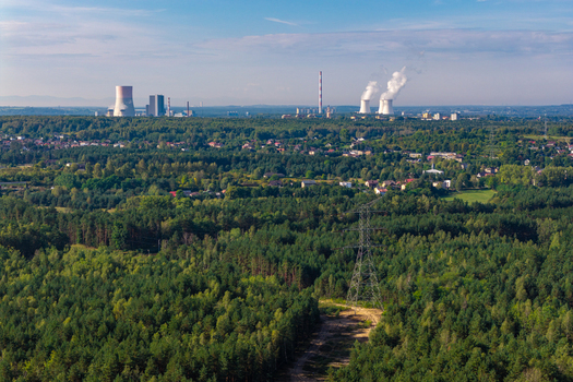 Aerial view of a large coal power plant with cooling towers and chimneys rising above a dense forest and suburban area in Katowice Silesian Voivodeship Poland.