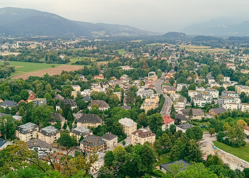 View of the historic city of Salzburg nestled among lush green trees and surrounded by rolling mountains under a soft overcast sky in Salzburg Salzburg Austria. View of the historic city of Salzburg nestled among lush green trees and surrounded by rolling mountains under a soft overcast sky in Salzburg Salzburg Austria.