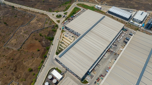 Aerial view of a large modern warehouse complex with expansive metal roofs parking areas and surrounding industrial infrastructure in Bhiwandi Maharashtra India. Aerial view of a large modern warehouse complex with expansive metal roofs parking areas and surrounding industrial infrastructure in Bhiwandi Maharashtra India.