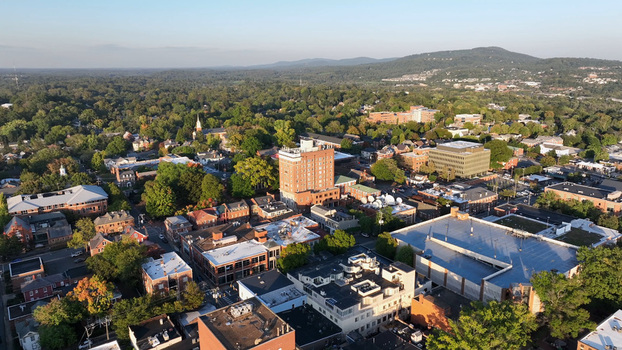Aerial view of the downtown area featuring historic buildings dense tree canopy and urban rooftops under a clear sky in Charlottesville Virginia United States.