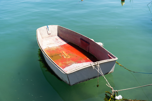 View of a small white rowboat with a red interior floating on calm turquoise water in Marsaskala Southern Region Malta. View of a small white rowboat with a red interior floating on calm turquoise water in Marsaskala Southern Region Malta.