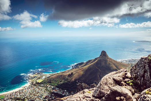 View of Lion s Head peak overlooking the Atlantic Ocean coastline with city buildings and rocky cliffs under a cloudy sky Cape Town Western Cape South Africa. View of Lion s Head peak overlooking the Atlantic Ocean coastline with city buildings and rocky cliffs under a cloudy sky Cape Town Western Cape South Africa.
