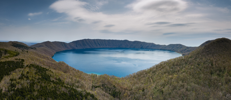 Aerial view of the deep blue waters of Lake Kuttara surrounded by forested caldera walls under a clear sky in Noboribetsu Hokkaido Japan. Aerial view of the deep blue waters of Lake Kuttara surrounded by forested caldera walls under a clear sky in Noboribetsu Hokkaido Japan.