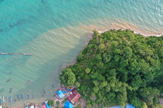 Aerial view of Pulau Maginti featuring lush green vegetation small wooden boats moored in turquoise coastal waters and a small settlement along the shore in Maginti South East Sulawesi Indonesia.