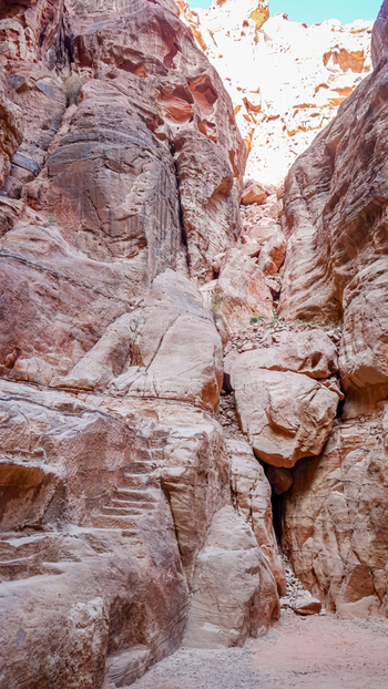 View of the narrow towering sandstone walls of the Siq featuring carved stone steps and rugged rock formations under bright daylight in Wadi Musa Ma an Governorate Jordan. View of the narrow towering sandstone walls of the Siq featuring carved stone steps and rugged rock formations under bright daylight in Wadi Musa Ma an Governorate Jordan.