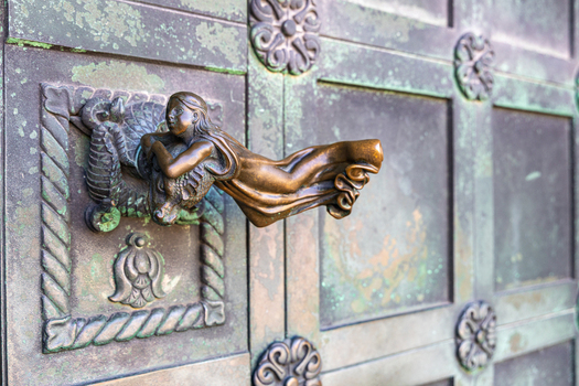 View of the ornate bronze door handle featuring a sculpted figure on the weathered green metal doors of Ribe Cathedral in Ribe Denmark. View of the ornate bronze door handle featuring a sculpted figure on the weathered green metal doors of Ribe Cathedral in Ribe Denmark.