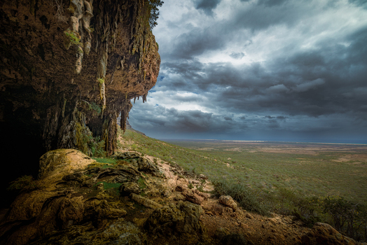 View of the entrance to the Da ira cave with hanging stalactites overlooking a vast landscape under a dramatic stormy sky in Da ira Socotra Yemen.