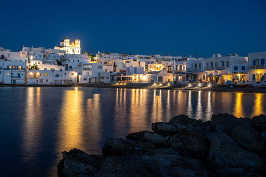 View of the illuminated coastal town of Lefkada at night with traditional white architecture a glowing church and warm lights reflecting on the calm sea. Lefkada Greece.