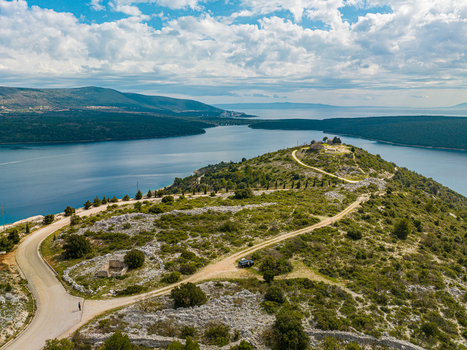 Aerial view of a winding road leading to a historic site atop a rugged peninsula embraced by the tranquil Adriatic Sea Rakalj Sv. Agnija Istria County Croatia.