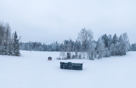 Aerial view of a small cabin and a barrel sauna situated in a vast snow covered field surrounded by a dense frost covered forest in Latvia. Aerial view of a small cabin and a barrel sauna situated in a vast snow covered field surrounded by a dense frost covered forest in Latvia.