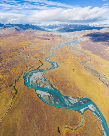 Aerial view of the Denali Highway winding through the vast Alaskan tundra with a turquoise braided river flowing through autumn colored landscapes in Cantwell Alaska United States.