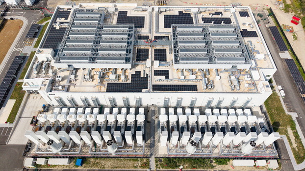 Aerial view of a modern data center campus with solar panels on the roof and industrial cooling infrastructure in Melegnano Lombardy Italy.