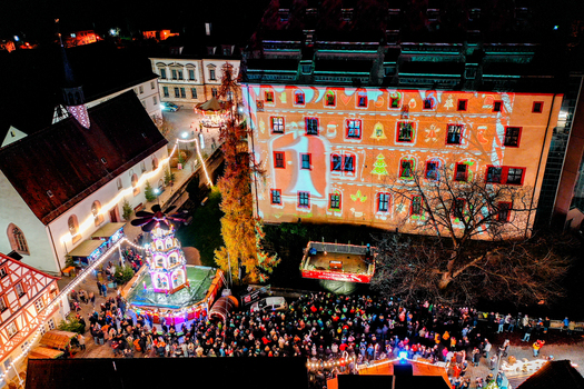 Forchheim Germany 20 December 2025 Aerial view of the Weihnachtsmarkt Forchheim with a festive light projection on the Kaiserpfalz building and a crowd of people at night.