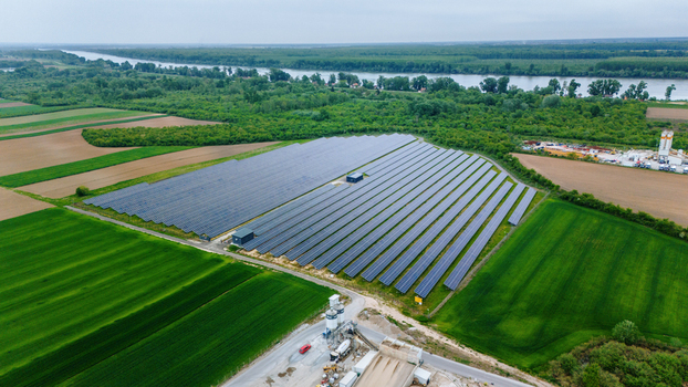 Aerial view of a large solar panel farm surrounded by lush green agricultural fields and dense forests near a river in Sabac Vojvodina Serbia.