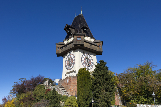 View of the historic clock tower perched atop a hill standing tall against the clear blue sky amidst lush greenery Graz Styria Austria. View of the historic clock tower perched atop a hill standing tall against the clear blue sky amidst lush greenery Graz Styria Austria.