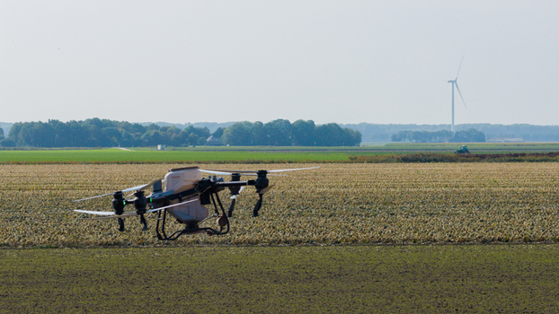 Aerial view of an agricultural drone flying over a cultivated field with a wind turbine in the distance in Zeewolde Flevoland Netherlands. Aerial view of an agricultural drone flying over a cultivated field with a wind turbine in the distance in Zeewolde Flevoland Netherlands.