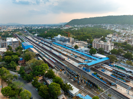 Aerial view of Udaipur Railway Station with passenger trains parked at platforms surrounded by urban buildings green trees and hills in Udaipur Rajasthan India. Aerial view of Udaipur Railway Station with passenger trains parked at platforms surrounded by urban buildings green trees and hills in Udaipur Rajasthan India.