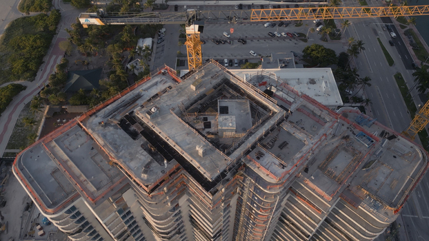 Aerial view of a high rise building under construction with a large yellow crane concrete structure and surrounding urban landscape in Miami Beach Florida United States. Aerial view of a high rise building under construction with a large yellow crane concrete structure and surrounding urban landscape in Miami Beach Florida United States.