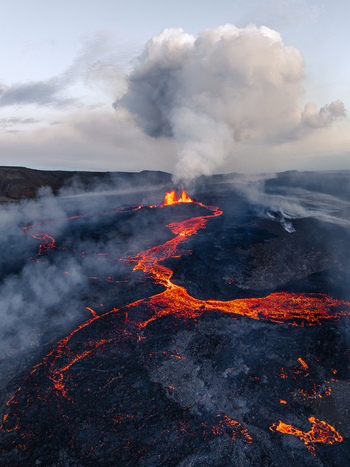 Aerial view of a volcanic eruption with glowing lava flows and thick smoke rising from the crater across the dark volcanic landscape in Iceland. Aerial view of a volcanic eruption with glowing lava flows and thick smoke rising from the crater across the dark volcanic landscape in Iceland.