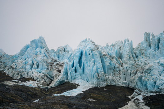 View of the Drygalski Fjord glacier with jagged blue ice formations and dark rocky terrain under an overcast sky in South Georgia and the South Sandwich Islands.