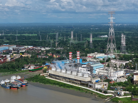 Aerial view of the power plant along the Karnaphuli River with cooling towers smokestacks and docked cargo ships in Chattogram Chattogram Division Bangladesh.