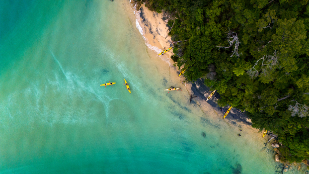 Aerial view of golden kayaks resting on a pristine beach where the lush forest meets the turquoise sea Abel Tasman National Park Tasman Region New Zealand. Aerial view of golden kayaks resting on a pristine beach where the lush forest meets the turquoise sea Abel Tasman National Park Tasman Region New Zealand.