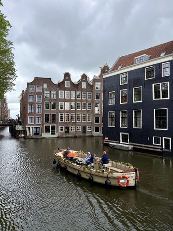 View of a canal boat with people cruising past traditional gabled houses under an overcast sky in Amsterdam Netherlands. View of a canal boat with people cruising past traditional gabled houses under an overcast sky in Amsterdam Netherlands.