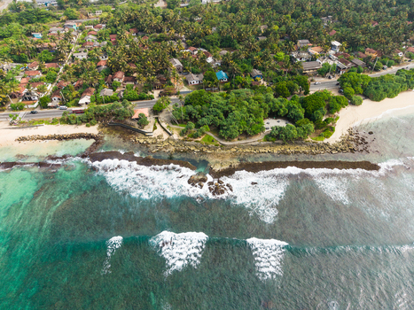 Aerial view of the tropical coastline with turquoise waves breaking against the shore and lush palm trees surrounding a coastal village in Koggala Southern Province Sri Lanka. Aerial view of the tropical coastline with turquoise waves breaking against the shore and lush palm trees surrounding a coastal village in Koggala Southern Province Sri Lanka.