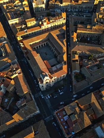 Aerial view of a historic monastery with a central courtyard and arched cloisters surrounded by terracotta rooftops during golden hour in Catania Sicily Italy. Aerial view of a historic monastery with a central courtyard and arched cloisters surrounded by terracotta rooftops during golden hour in Catania Sicily Italy.