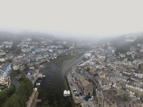 Aerial view of the coastal town of Looe featuring the river estuary historic buildings and small boats docked along the banks under morning fog in Looe Cornwall United Kingdom. Aerial view of the coastal town of Looe featuring the river estuary historic buildings and small boats docked along the banks under morning fog in Looe Cornwall United Kingdom.