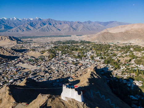 Aerial view of Leh Palace and the surrounding town nestled in the high altitude desert landscape of the Himalayas with snow capped peaks in the distance Leh Ladakh India. Aerial view of Leh Palace and the surrounding town nestled in the high altitude desert landscape of the Himalayas with snow capped peaks in the distance Leh Ladakh India.