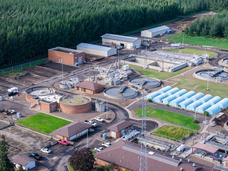 Aerial view of a wastewater treatment plant featuring circular sedimentation tanks blue storage structures and industrial buildings in Woodburn Oregon United States. Aerial view of a wastewater treatment plant featuring circular sedimentation tanks blue storage structures and industrial buildings in Woodburn Oregon United States.