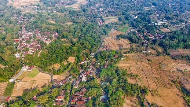 Aerial view of Karangrejo village surrounded by lush tropical trees terraced rice fields and a winding road in the rural landscape. Borobudur Central Java Indonesia.