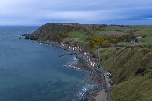 Aerial view of Crovie fishing village nestled at the foot of steep green cliffs along the rugged North Sea coast Crovie Scotland United Kingdom.