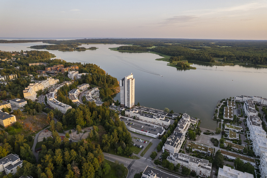Aerial view of Kivenlahti featuring modern residential buildings a tall apartment tower lush forests and the calm waters of the Gulf of Finland in Espoo Uusimaa Finland.
