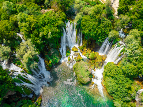 Aerial view of Kravica Waterfall cascading into a turquoise pool surrounded by lush green trees and rocky formations in Zvirici Federation of Bosnia Bosnia and Herzegovina. Aerial view of Kravica Waterfall cascading into a turquoise pool surrounded by lush green trees and rocky formations in Zvirici Federation of Bosnia Bosnia and Herzegovina.