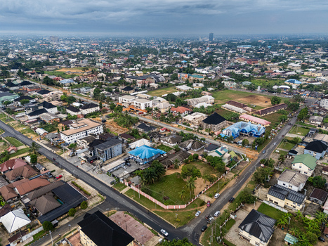 Aerial view of a sprawling urban landscape under a soft cloudy sky where diverse structures with contrasting roofs intermingle with lush green spaces Uyo Akwa Ibom Nigeria. Aerial view of a sprawling urban landscape under a soft cloudy sky where diverse structures with contrasting roofs intermingle with lush green spaces Uyo Akwa Ibom Nigeria.