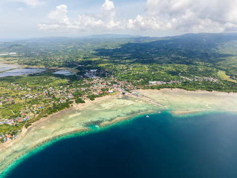 Aerial view of the coastal town featuring vibrant coral reefs turquoise waters and lush tropical vegetation under a cloudy sky Moalboal Central Visayas Philippines.