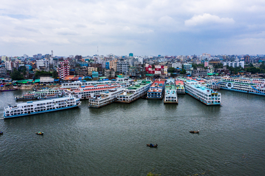 Aerial view of numerous passenger ferries docked at the busy river port with the dense urban skyline of Dhaka in the background under a cloudy sky in Dhaka Dhaka Division Bangladesh.