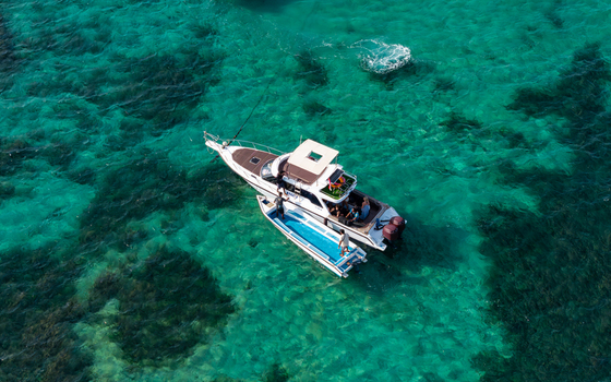 Aerial view of a motorboat and a smaller tender boat floating in clear turquoise water with visible seabed patterns in Kecamatan Denpasar Selatan Bali Indonesia.