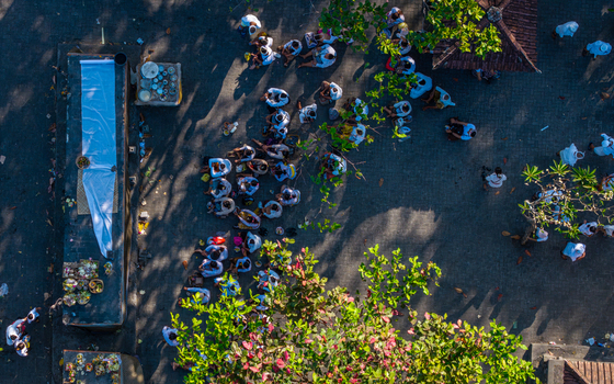 Aerial view of the Ngelarung Sea Offering Ceremony at Pura Segara Goa Lawah with people in traditional attire gathered on temple grounds in Dawan Bali Indonesia.