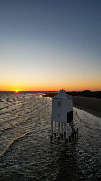Aerial view of the historic Burnham on Sea Low Lighthouse standing on wooden stilts in the water at sunset with gentle waves and a sandy beach in Burnham on Sea England United Kingdom. Aerial view of the historic Burnham on Sea Low Lighthouse standing on wooden stilts in the water at sunset with gentle waves and a sandy beach in Burnham on Sea England United Kingdom.